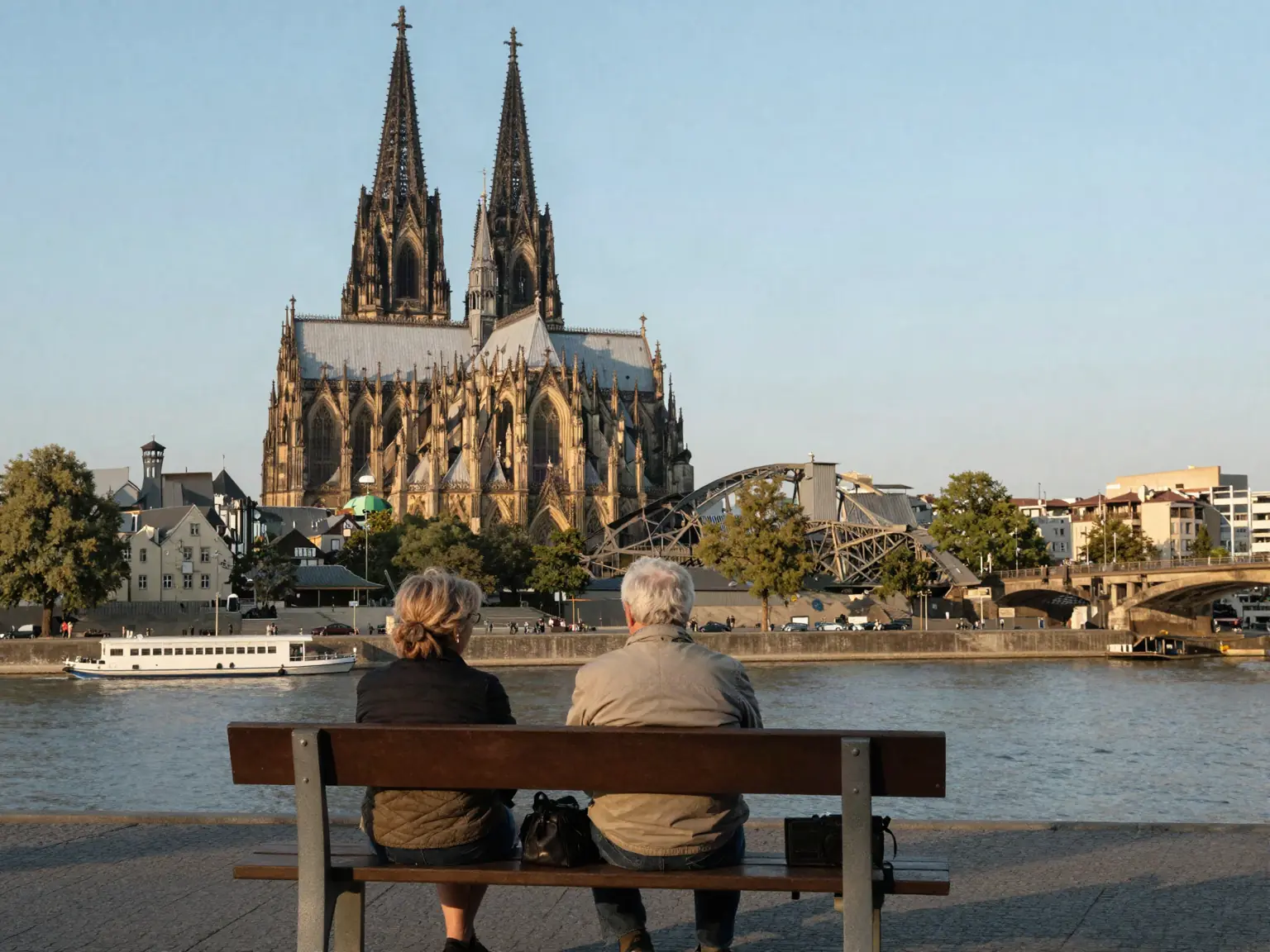 Älteres Paar sitzt auf einer Bank am Rheinufer, im Hintergrund der Kölner Dom